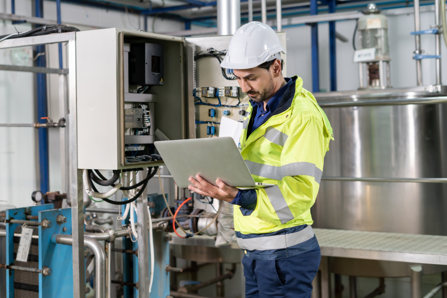 Maintenance technician E regelt met laptop elektrische besturingskast in bij industrieel proces